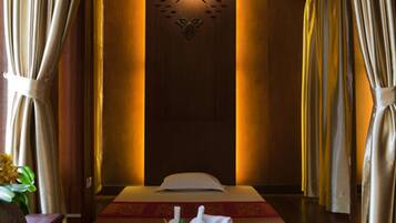 A spa room with a massage table, a decorative wall, and curtains.