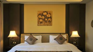 A hotel room with a large bed, two bedside lamps, a headboard with a floral pattern, and a wall-mounted artwork of flowers.