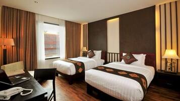 A hotel room with two beds, a desk with a telephone, and a window with curtains.