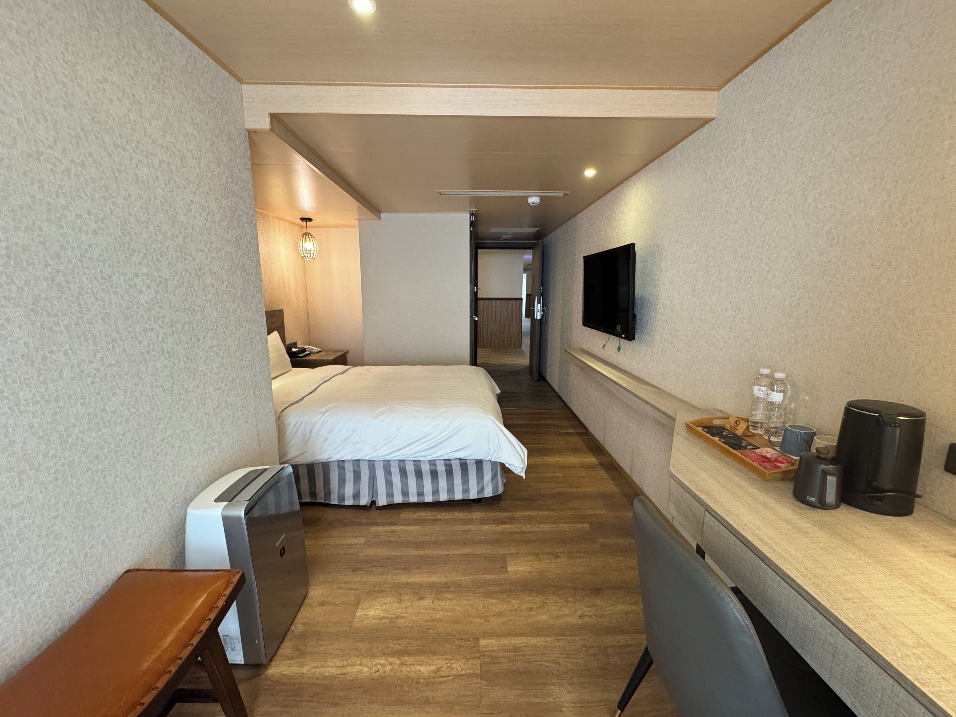 A hotel room with a bed, a desk with a coffee maker, a TV, and a small seating area.