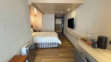 A hotel room with a bed, a desk with a coffee maker, a TV, and a small seating area.