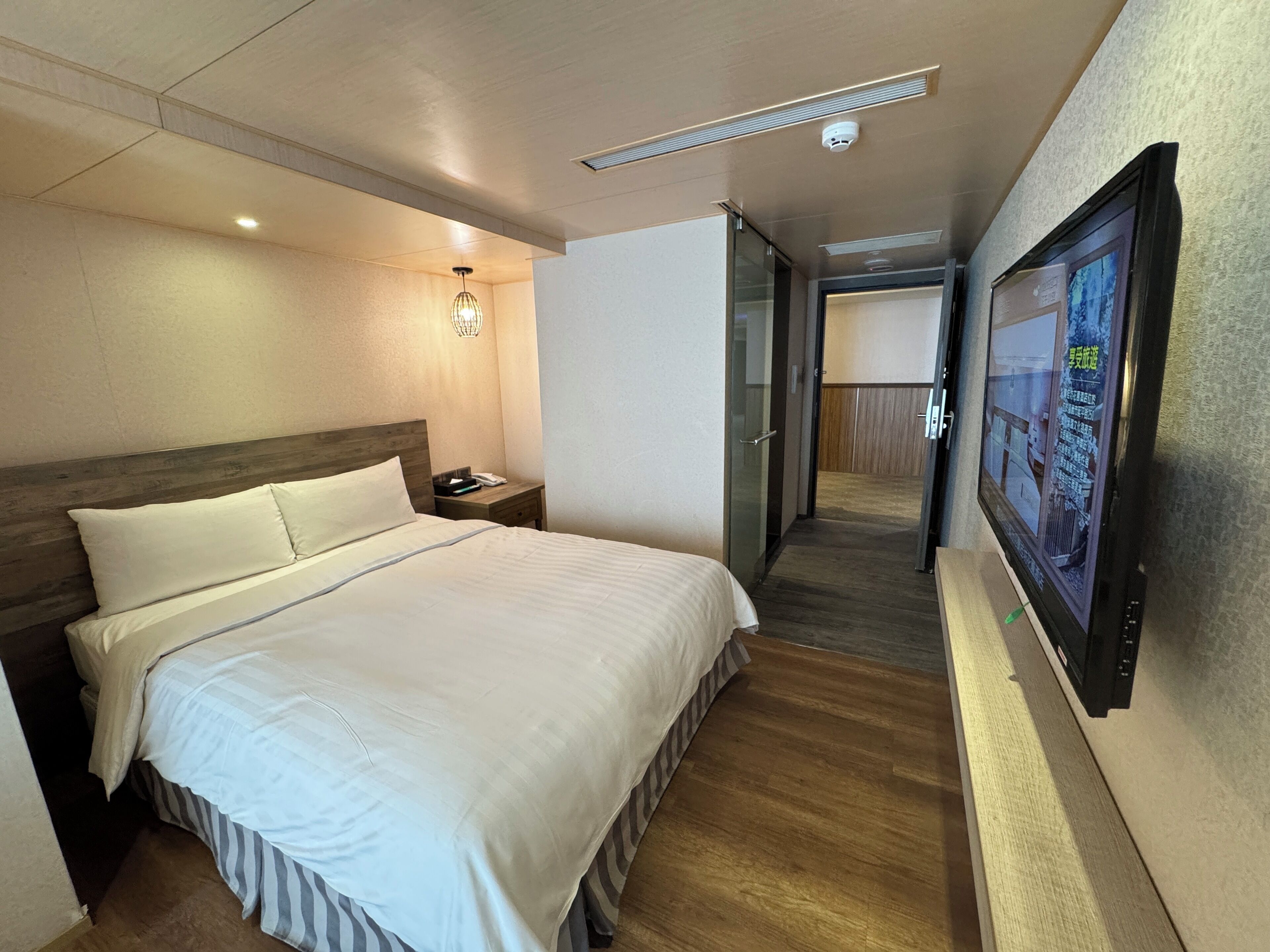 A hotel room with a large bed, bedside table, lamp, and a TV mounted on the wall.