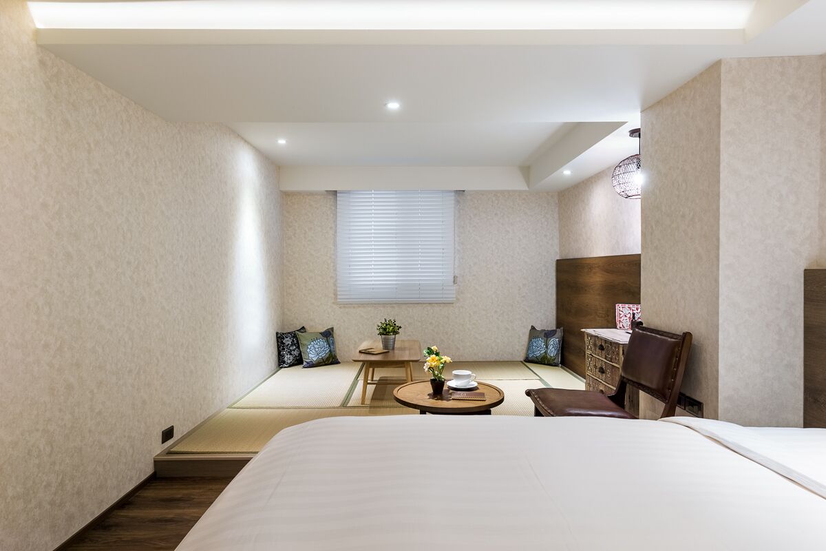 Una habitación de hotel moderna con una cama, una mesita con un florero, una silla, un escritorio y una ventana con persianas.