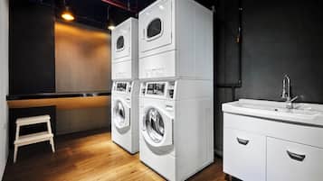 A laundry room with stacked washers and dryers, a sink, and a wooden floor.