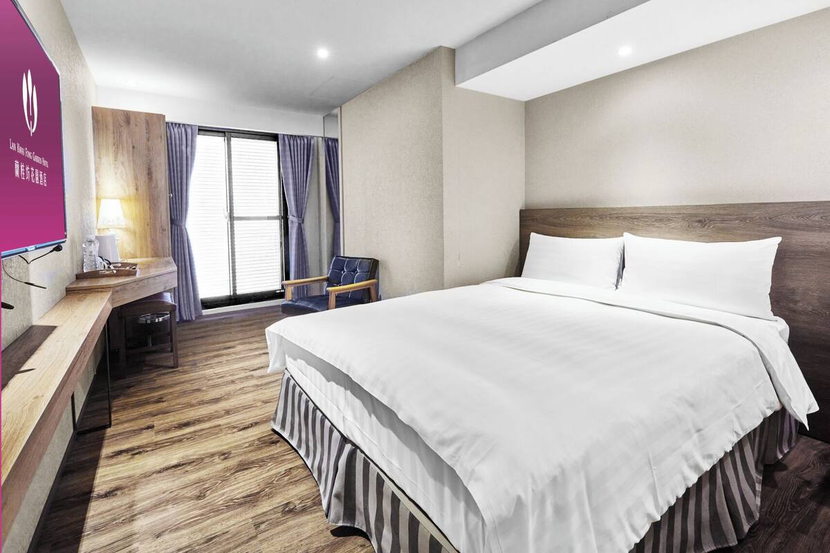 A hotel room with a large bed, a wooden desk, a chair, and a TV.