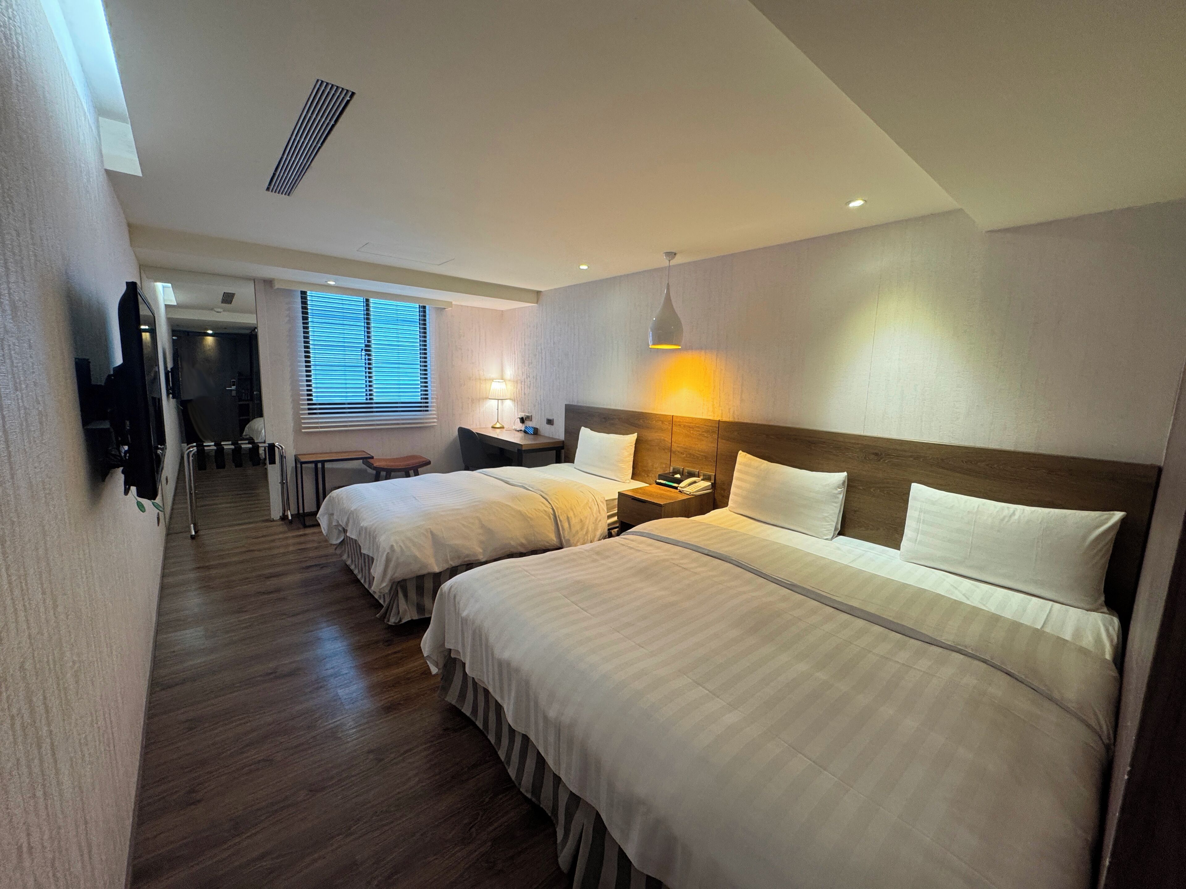 Habitación de hotel con dos camas, un escritorio, una silla, una lámpara y un televisor.
