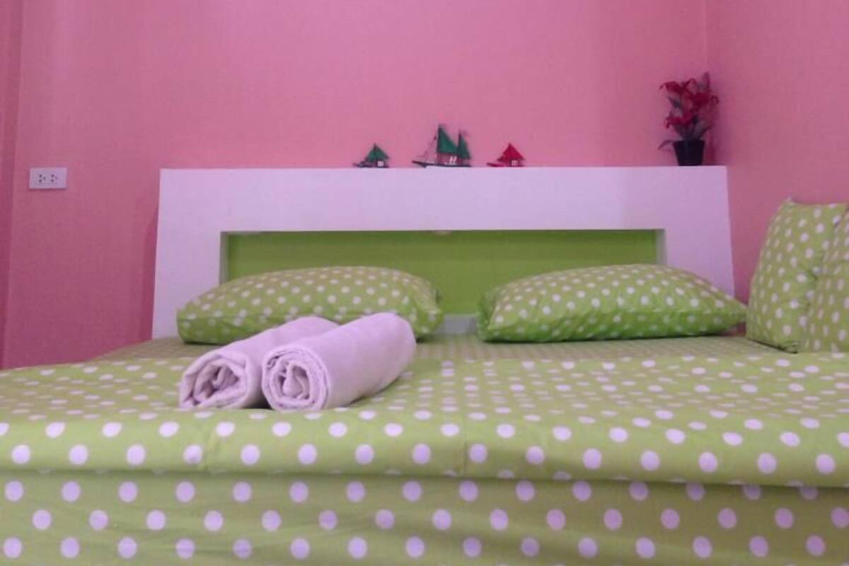 A bedroom with pink walls, a green polka dot bedspread, and a white air conditioner.