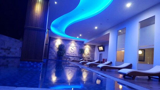 A modern indoor pool area with lounge chairs, a reception desk, and a stone wall with a logo. - The Safin Hotel Pati (Pati)