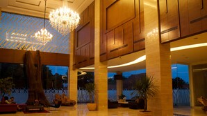 A spacious lobby with a large wooden tree trunk centerpiece, a chandelier, and potted plants. - The Safin Hotel Pati (Pati)
