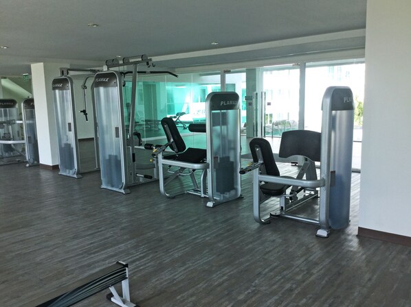 A gym with various exercise machines, large windows, and a modern interior design. - Amazon Residence by PSR ASIA (Pattaya)