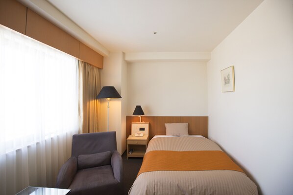 A hotel room with a bed, a chair, a nightstand with a lamp, and a window with curtains. - Hotel Granmirage (Uozu)