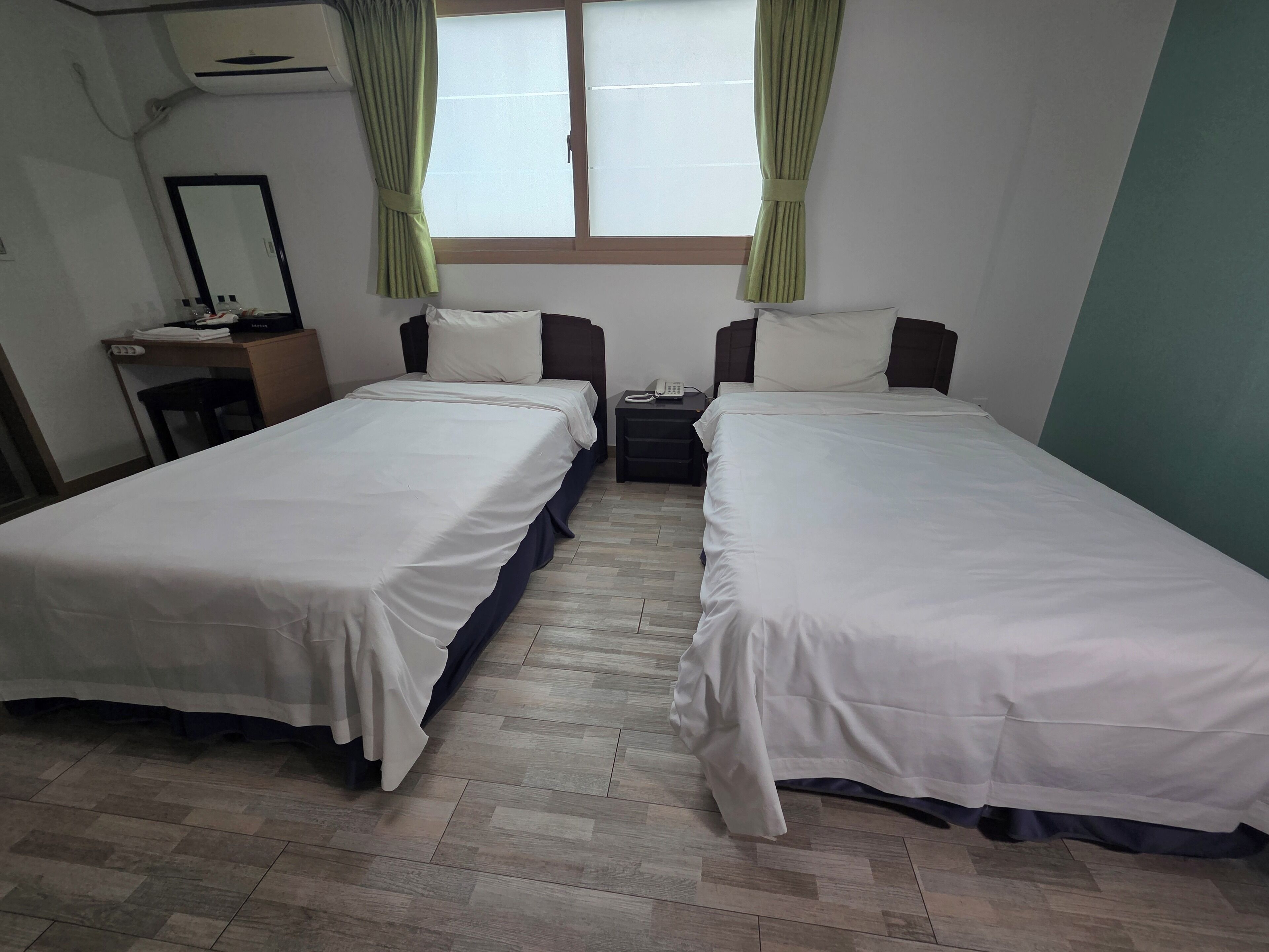 Quarto duplo com duas camas, uma escrivaninha, uma cadeira, um espelho e uma janela com cortinas.