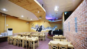 A restaurant with wooden tables and chairs, a stage with musical instruments, and a brick wall.