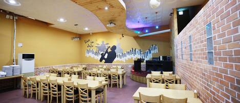 Ein Restaurant mit Holztischen und -stühlen, einer Bühne mit Musikinstrumenten und einer Ziegelwand.