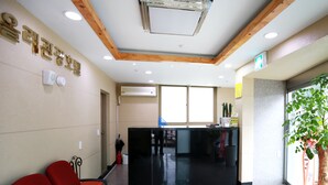 A reception area with a black reception desk, red chairs, a potted plant, and a wooden ceiling.