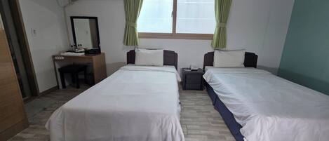Una camera d'albergo con due letti singoli, una scrivania con una sedia, uno specchio e una finestra con tende.