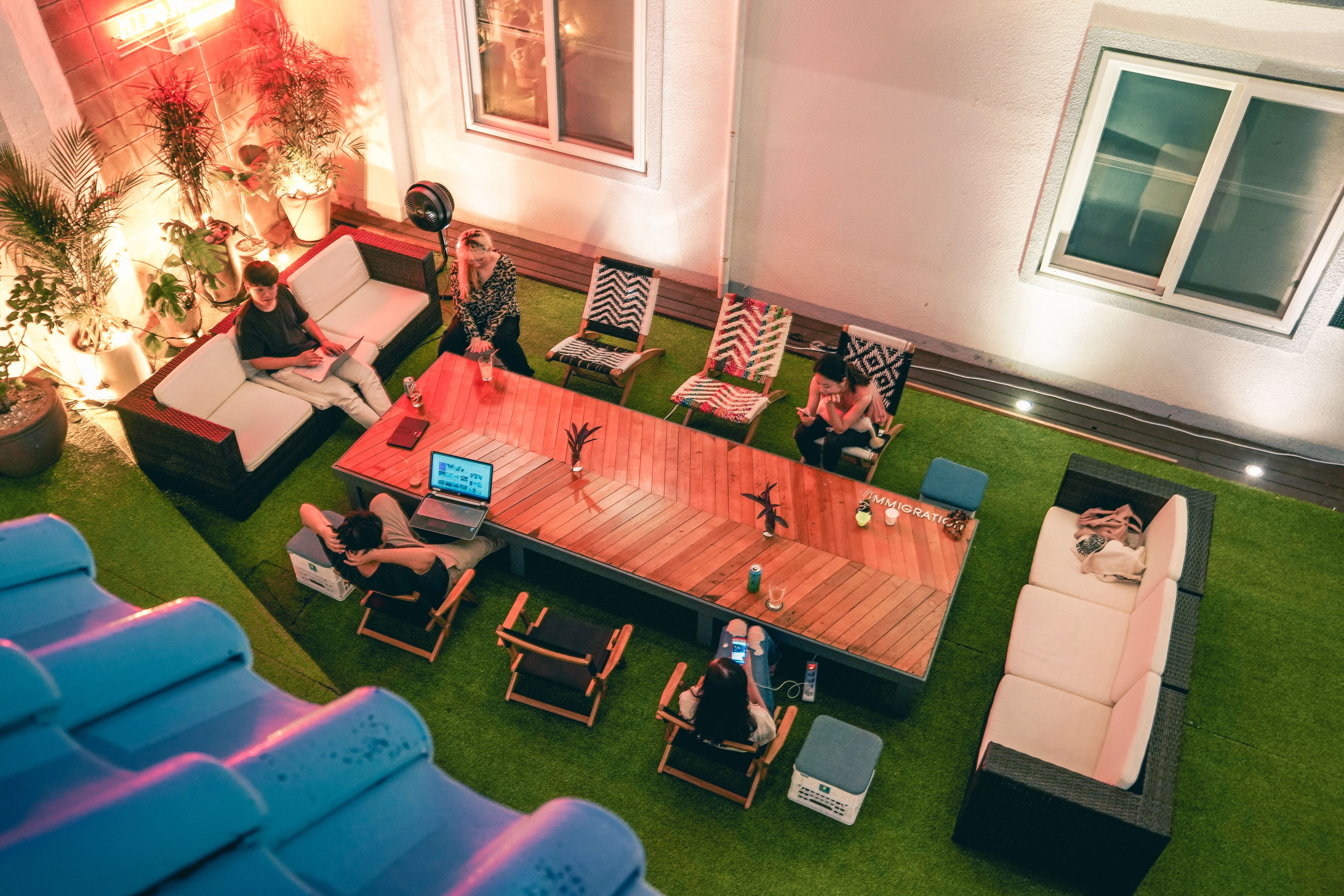 Un espace de détente extérieur moderne, avec une longue table en bois entourée de chaises, d’un canapé et d’une petite scène.