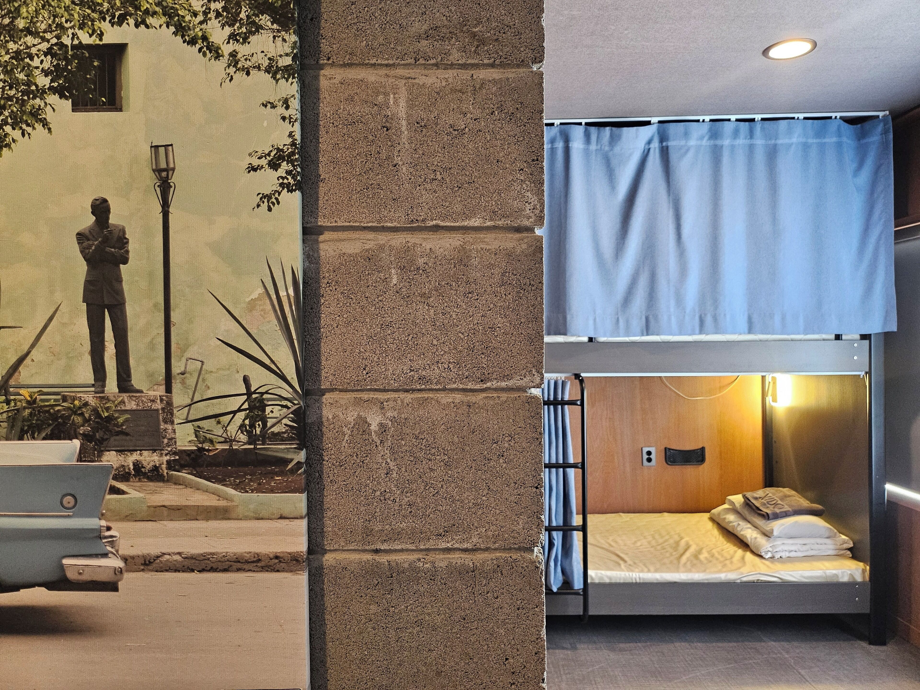 A bunk bed with a blue curtain, a small table with a lamp, and a statue in the foreground.