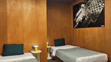 A hotel room with two single beds, wooden walls, a large black and white photo on the wall, and a ceiling light.