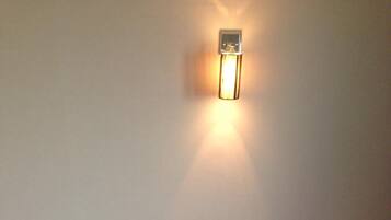 A room with two single beds, a small bedside table with a tissue box, and a wall-mounted light fixture.