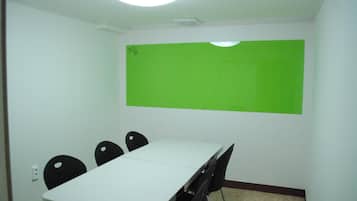 A conference room with a white table, four black chairs, and a green screen on the wall.
