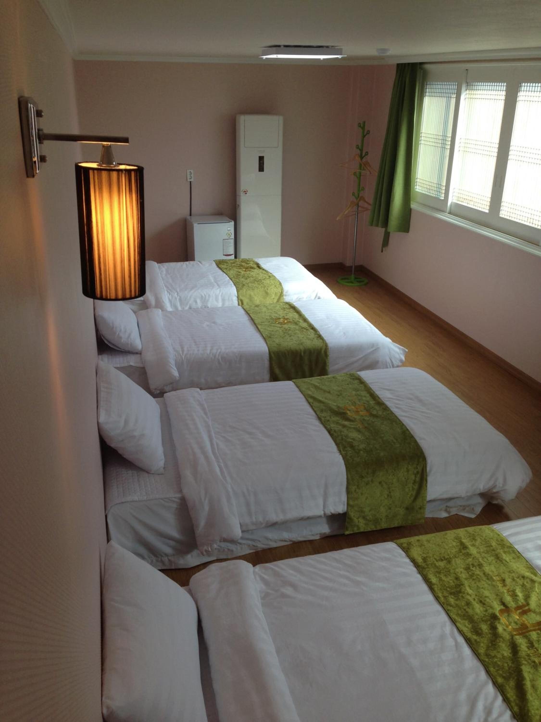 Habitación de hotel con dos camas, una lámpara de noche, un mueble pequeño y un ventanal con cortinas.