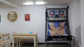 A room with a basketball hoop labeled "Pro Court 2," a wooden table, chairs, a wall clock, and a small decorative item.