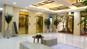 A modern lobby with a polished floor, a reception desk, and potted plants.