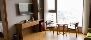Una habitación de hotel moderna con un escritorio de madera, un televisor de pantalla plana, un refrigerador pequeño y un área de comedor con dos sillas.