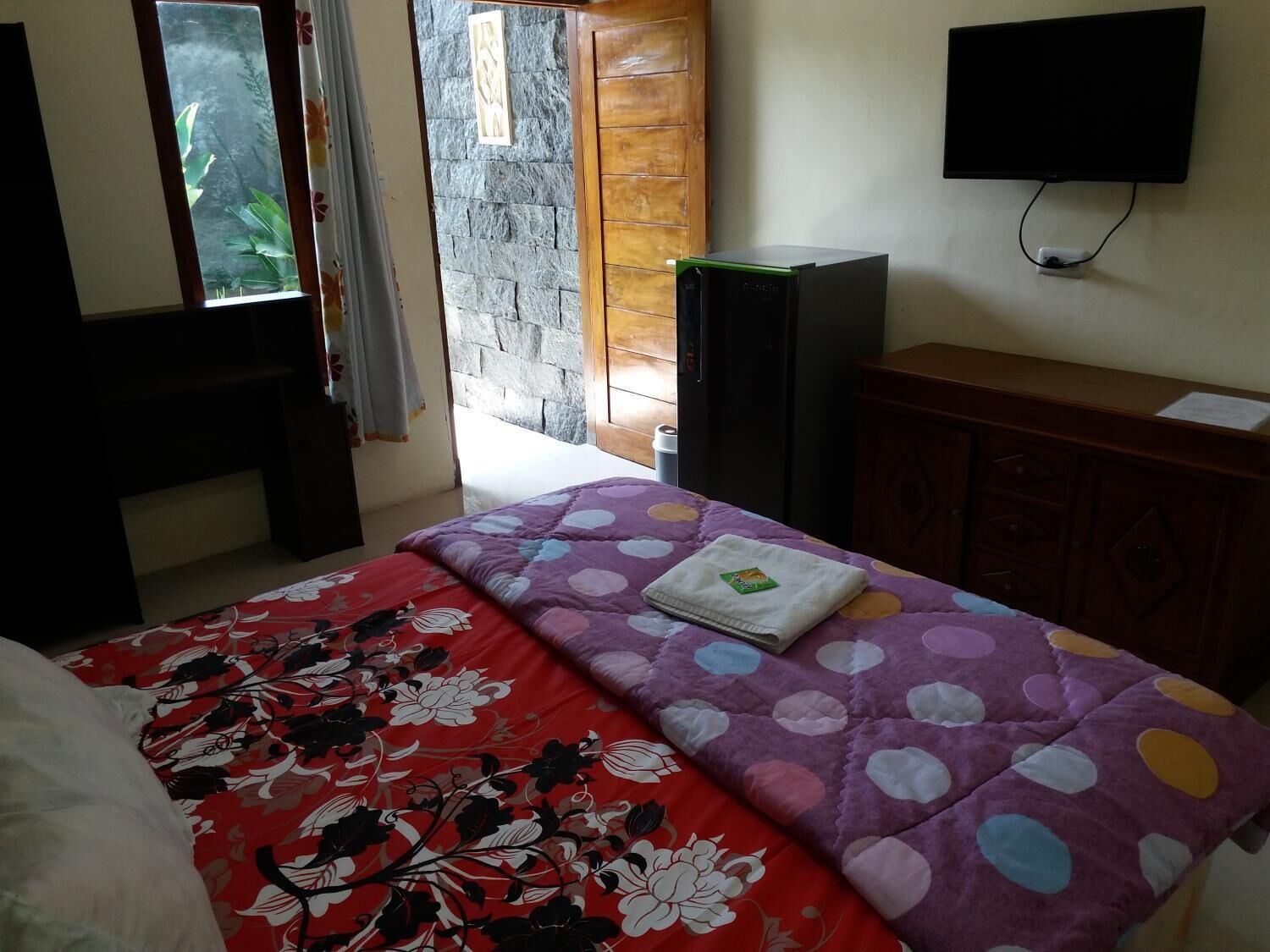 A bedroom with a bed, a TV, a wardrobe, and a window with curtains.