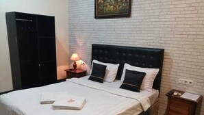 A neatly made bed with white linens and black pillows, a bedside table with a lamp, and a small wooden nightstand with a paper on it.