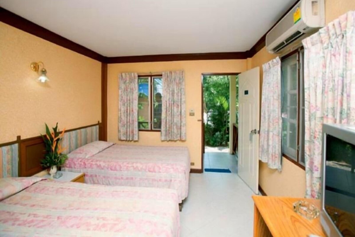 A hotel room with two beds, a wooden headboard, a television, and an air conditioning unit.