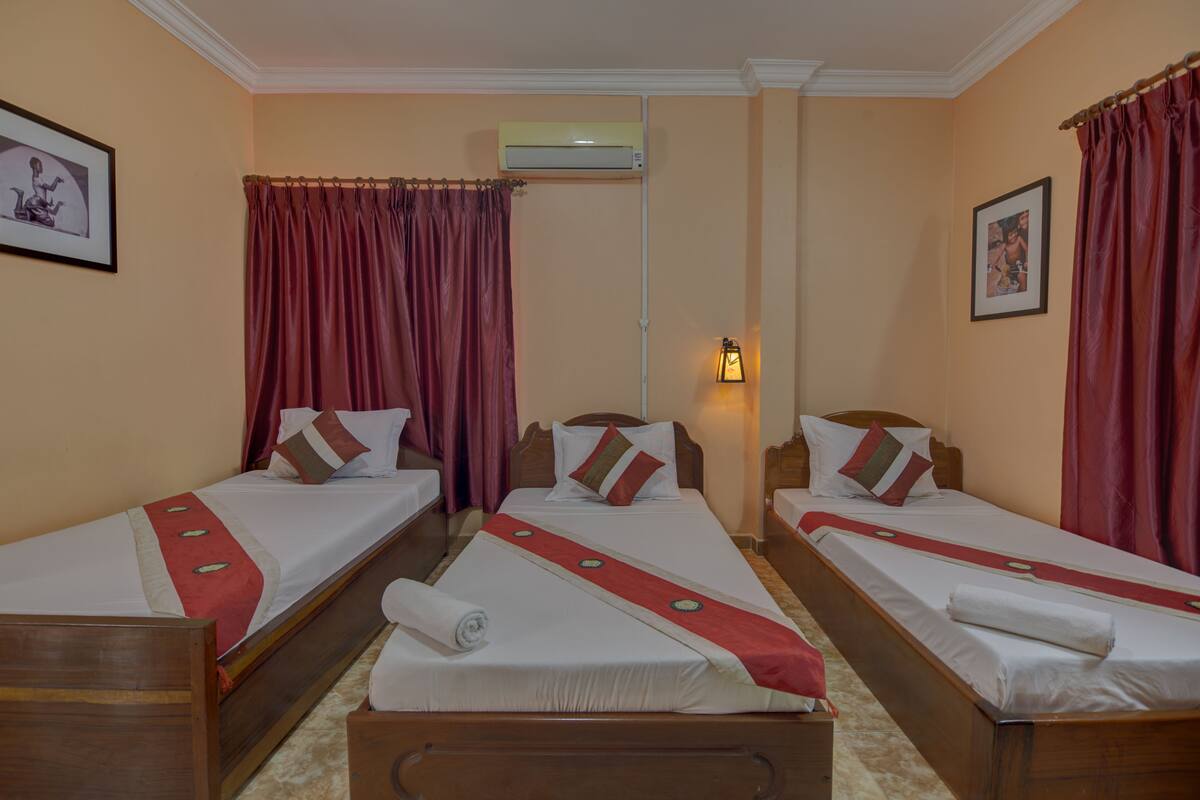 Une chambre d’hôtel avec deux lits simples, chacun recouvert d’une courtepointe rouge et blanche, dotée d’une tête de lit en bois et d’une petite table de chevet.