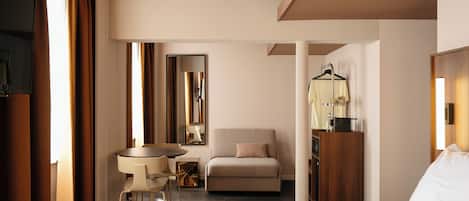 Ein Hotelzimmer mit einem Bett, einem Schreibtisch, einem Sessel, einem Sofa, einem Spiegel und einem Kleiderschrank.
