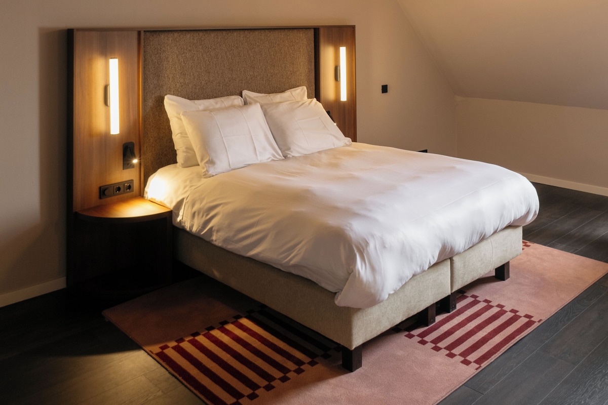A bedroom with a bed, wooden headboard, nightstands, and a hanging light fixture.