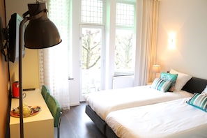 A hotel room with two beds, a desk with a lamp, and a window with curtains.