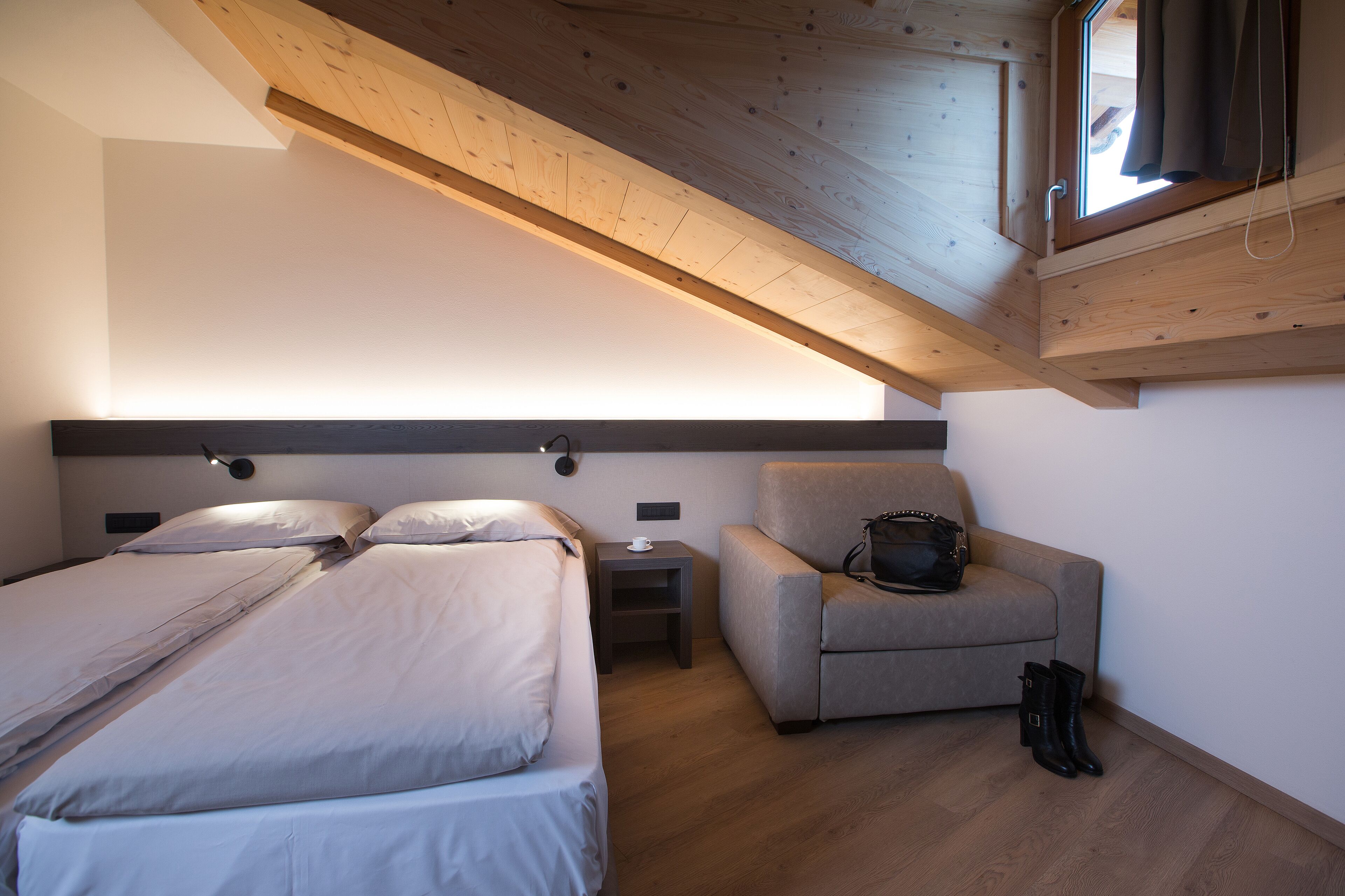 A bedroom with two beds, a nightstand, a chair, and a wooden ceiling.