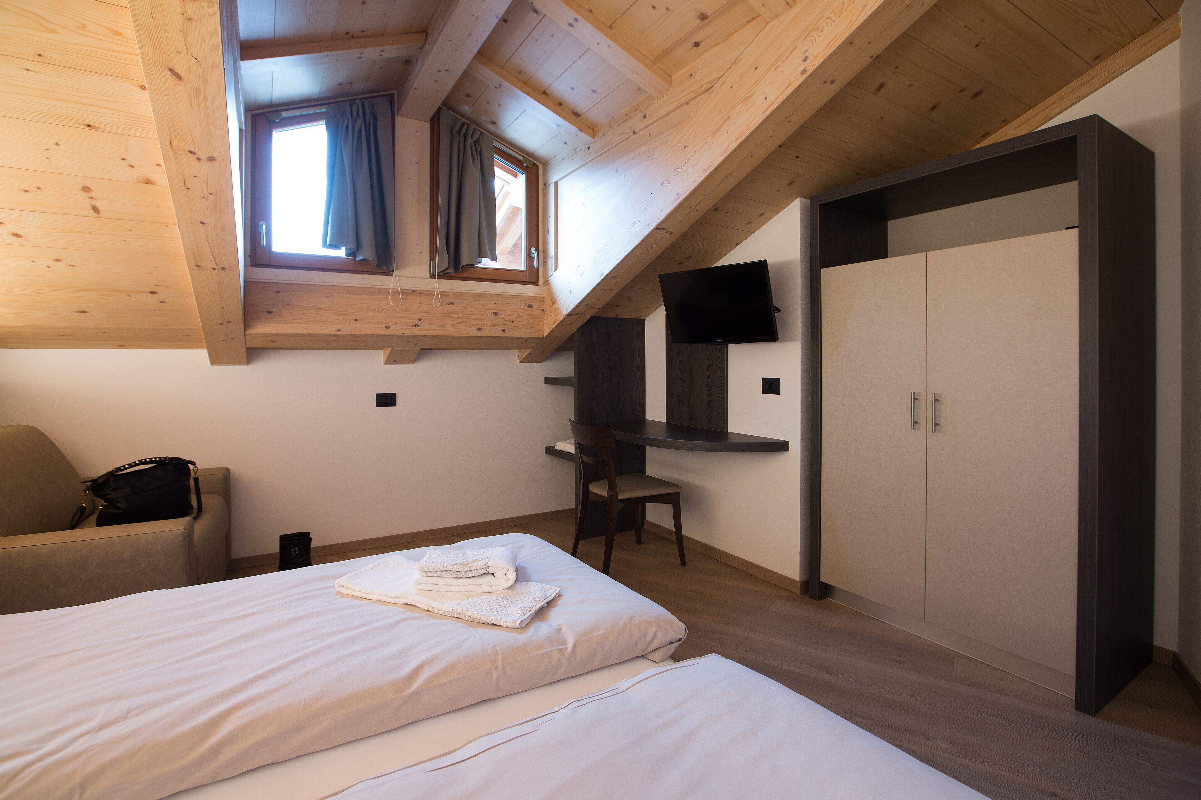 Een slaapkamer met twee bedden, een bureau, een stoel, een kledingkast en een aan de muur bevestigde televisie.