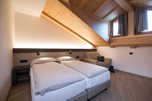 Un dormitorio con techo inclinado, dos camas, una mesita de noche, una silla y una ventana con cortinas.