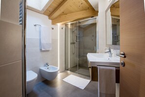 Une salle de bain moderne avec une douche à parois de verre, un bidet, des toilettes et un lavabo avec un miroir.