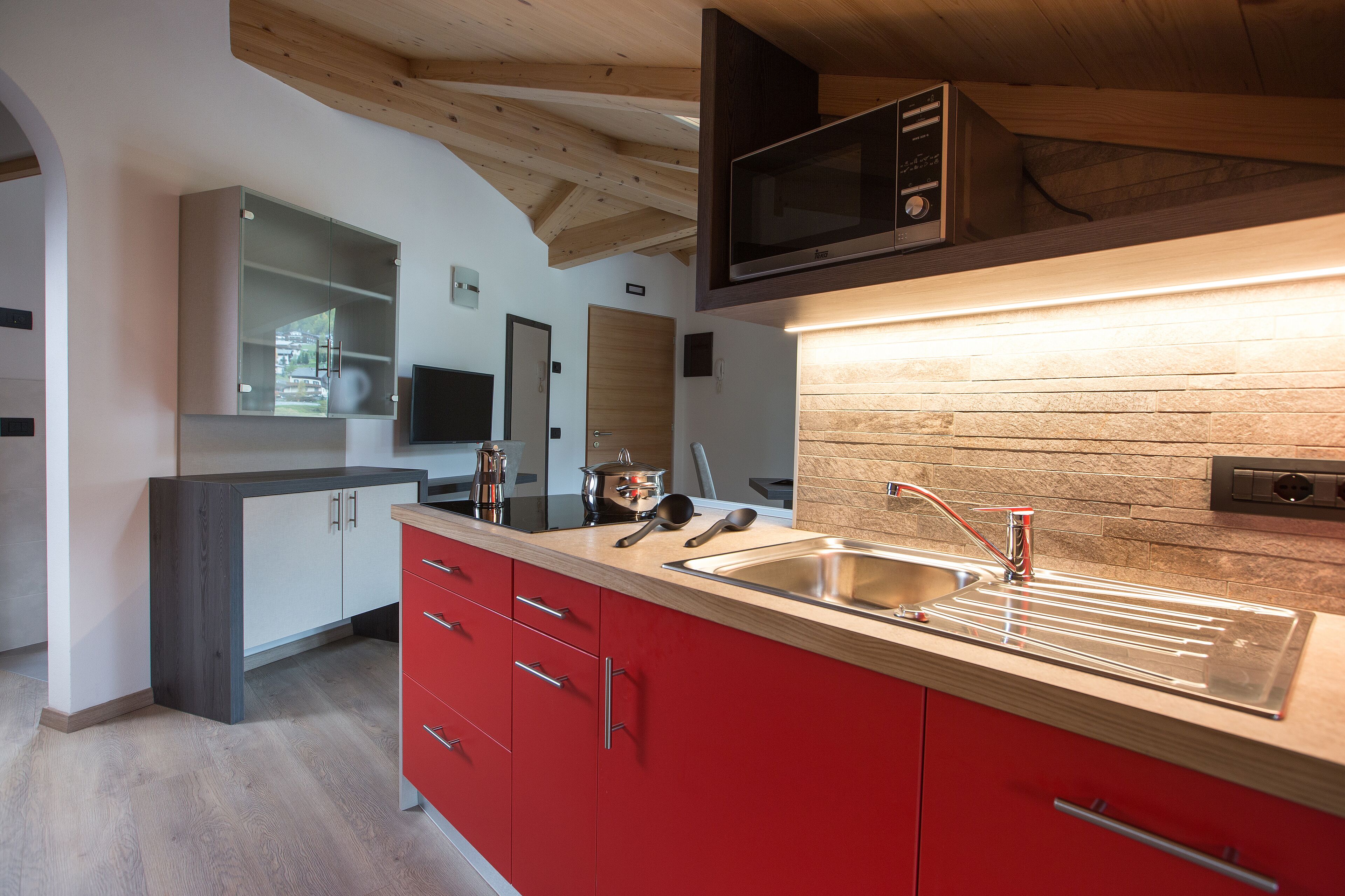 A modern kitchen with a wooden ceiling, a built-in microwave, a stainless steel sink, and red cabinets.