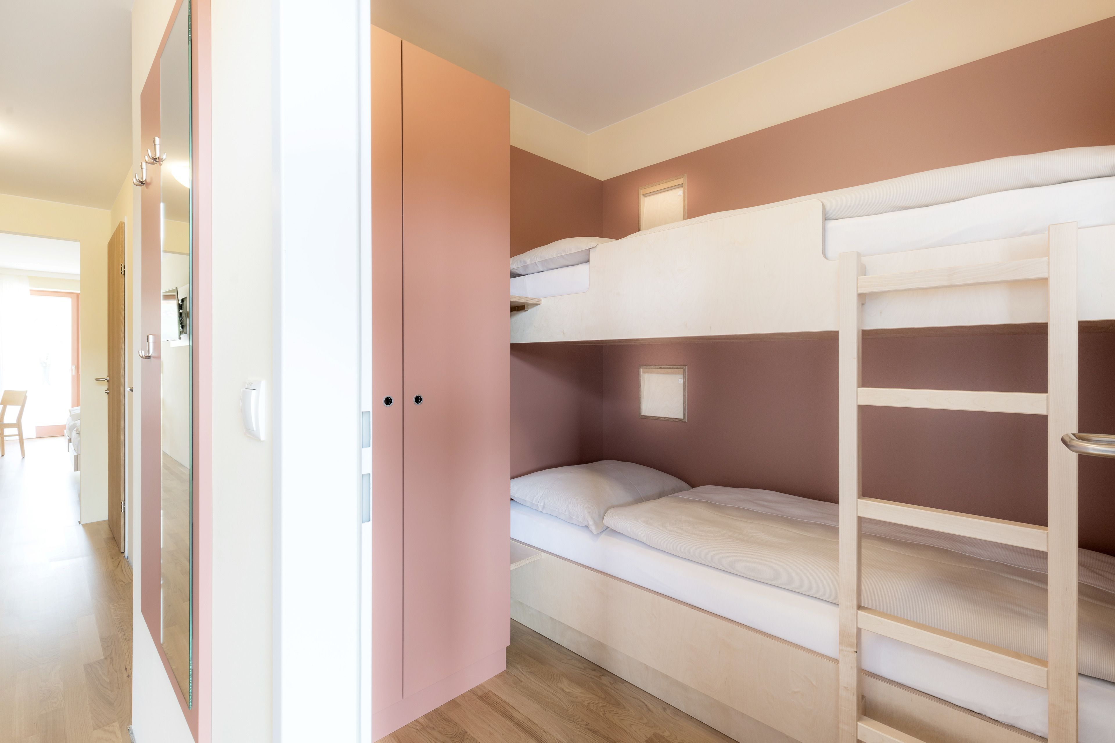 Habitación con literas, un armario rosa y suelo de madera.