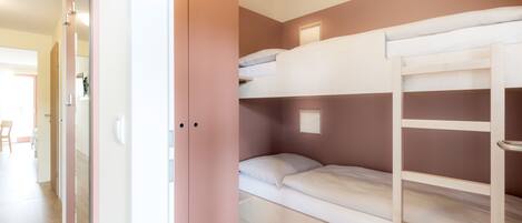 Habitación con literas, un armario rosa y suelo de madera.