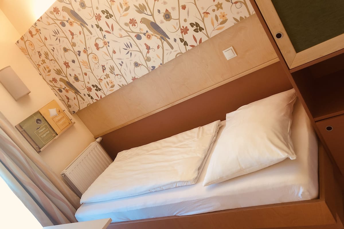 A neatly made bed with white linens in a room with wooden headboard and a floral-patterned wall.