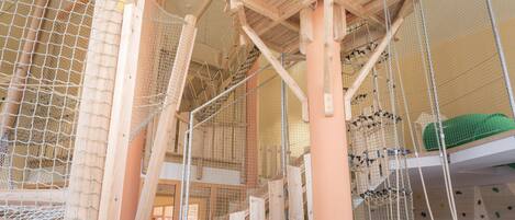 Instalación de escalada en interiores con muros de escalada de madera y una torre de observación con red.