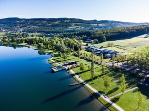 An aerial view of a lakeside property with a dock, a large building with a blue roof, and surrounding greenery. - JUFA Hotel Stubenbergsee (Stubenberg)