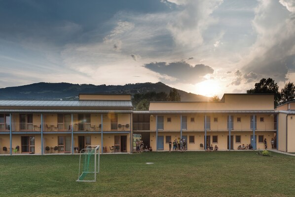 A multi-story building with a courtyard, a soccer goal, and a mountainous backdrop. - JUFA Hotel Stubenbergsee (Stubenberg)
