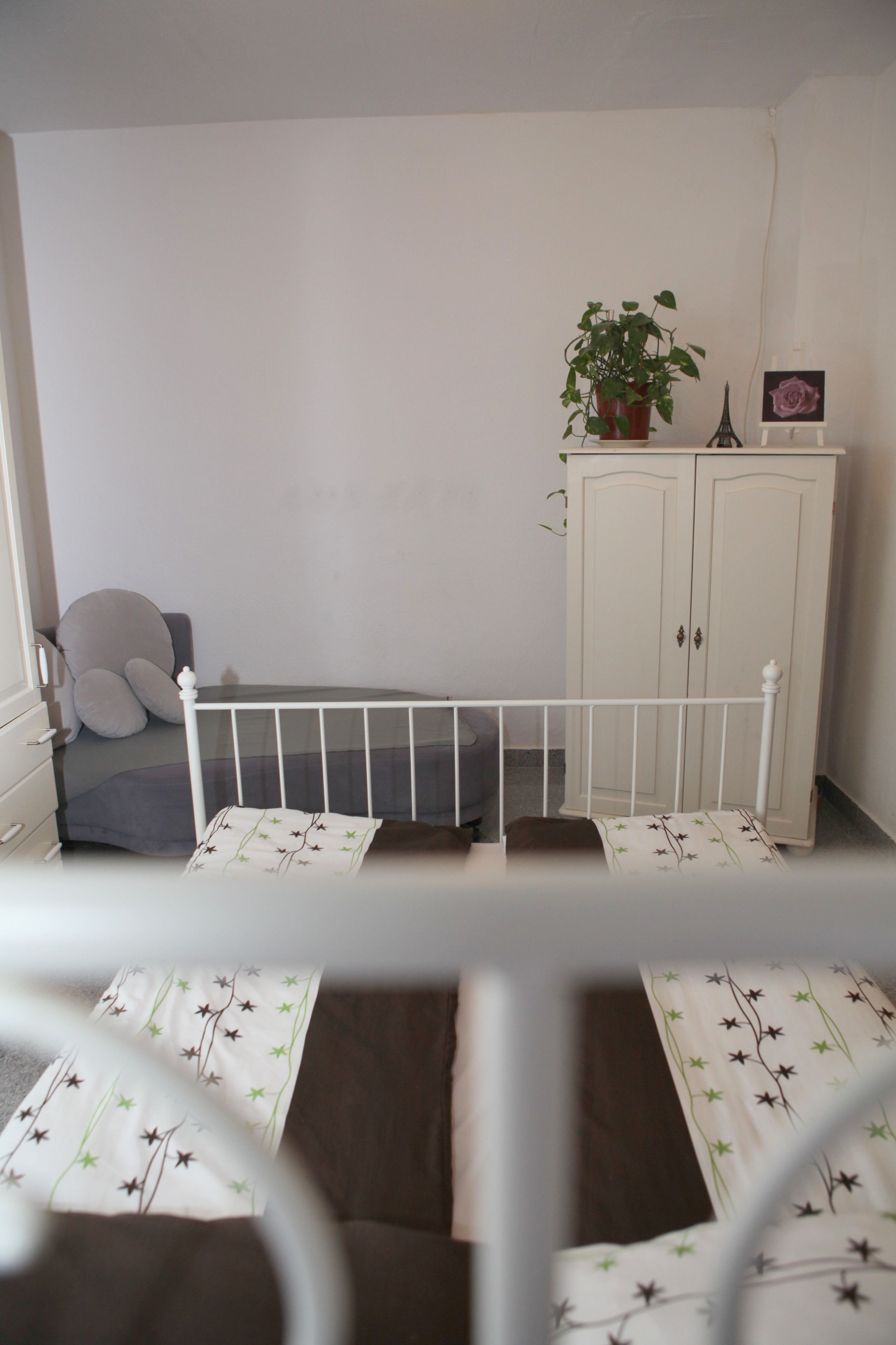 A bedroom with a crib, a wardrobe, a potted plant, and a picture of the Eiffel Tower.