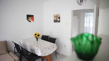 A dining area with a round table, chairs, and a vase with sunflowers. There are two framed pictures on the wall.