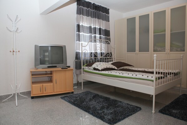 Une chambre à coucher avec un lit, un téléviseur posé sur un meuble, une armoire et un porte-manteau.